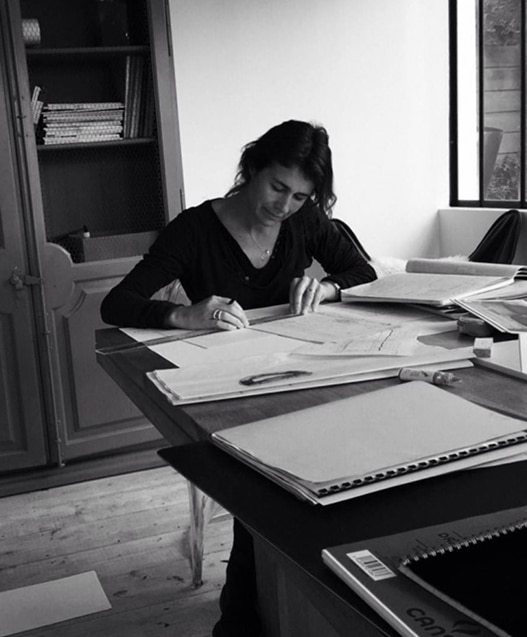 Femme concentrée dessinant avec une règle sur un plan technique, bureau en bois avec papiers et cahiers CANSON. N&B.
